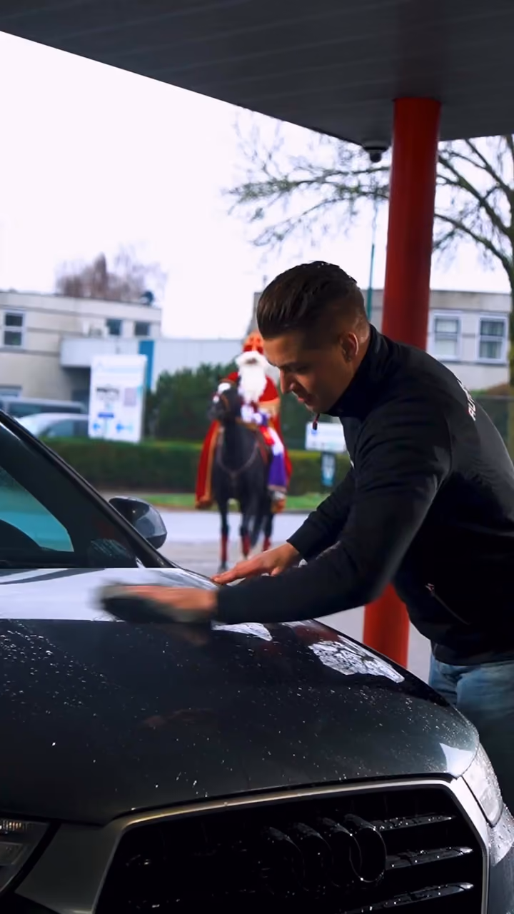 Medewerker poetst de motorkap, Sinterklaas te paard op de achtergrond