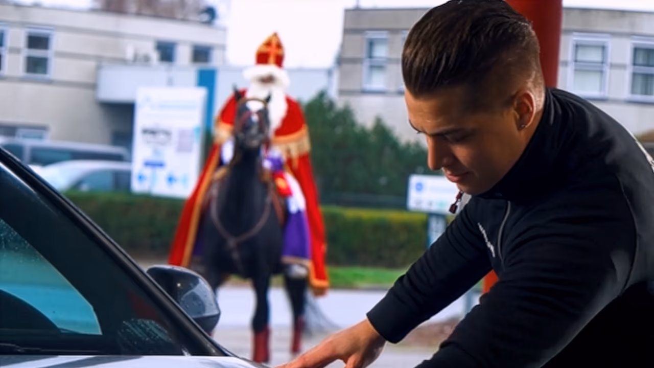 Medewerker poetst een auto terwijl Sinterklaas op zijn paard op de achtergrond toekijkt