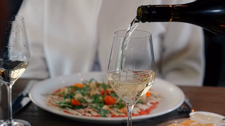 Witte wijn wordt ingeschonken naast een bord carpaccio op tafel