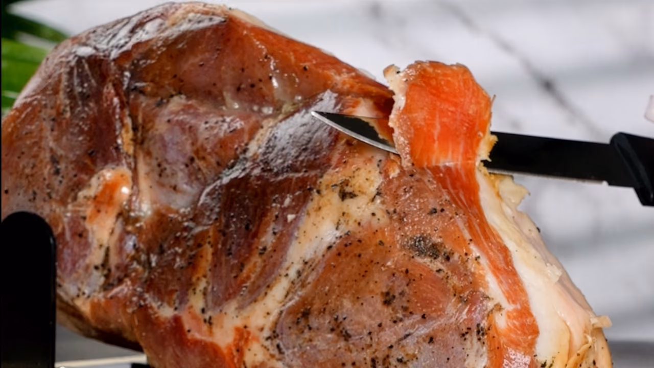 Close-up van een Spaanse mini-ham waar met een mes een dunne plak vanaf wordt gesneden