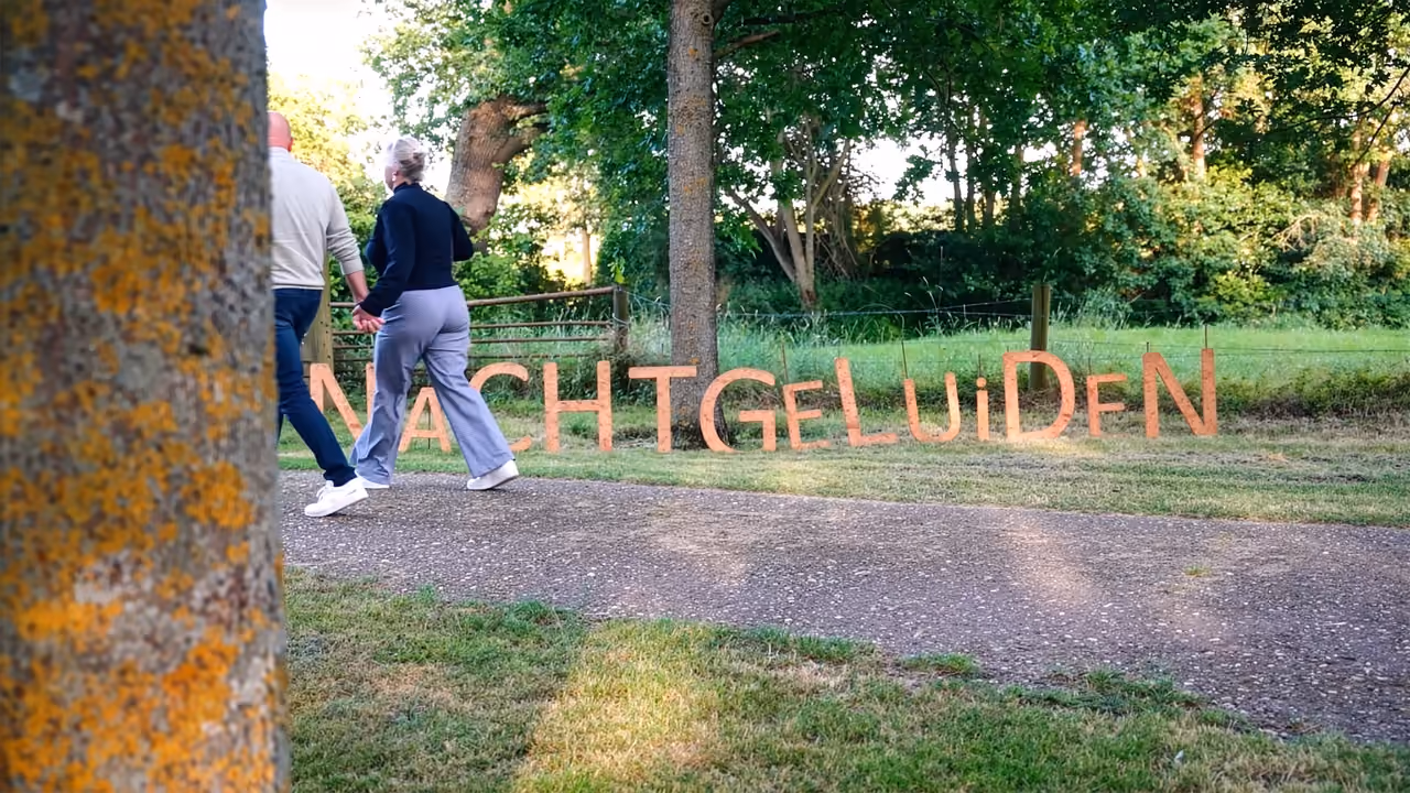 Twee bezoekers lopen hand in hand langs houten letters die Nachtgeluiden spellen in het gras